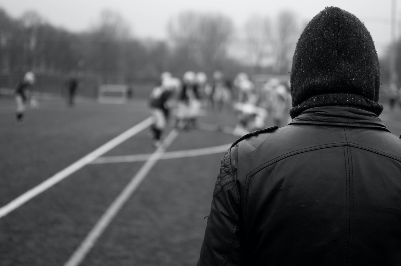 Hooded football hooligan faces away from the camera at a football team.