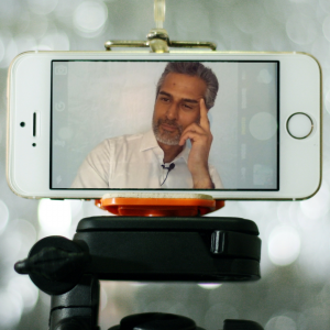 A tripod holding a phone on which is displayed Kal Sabir in a remote meeting.