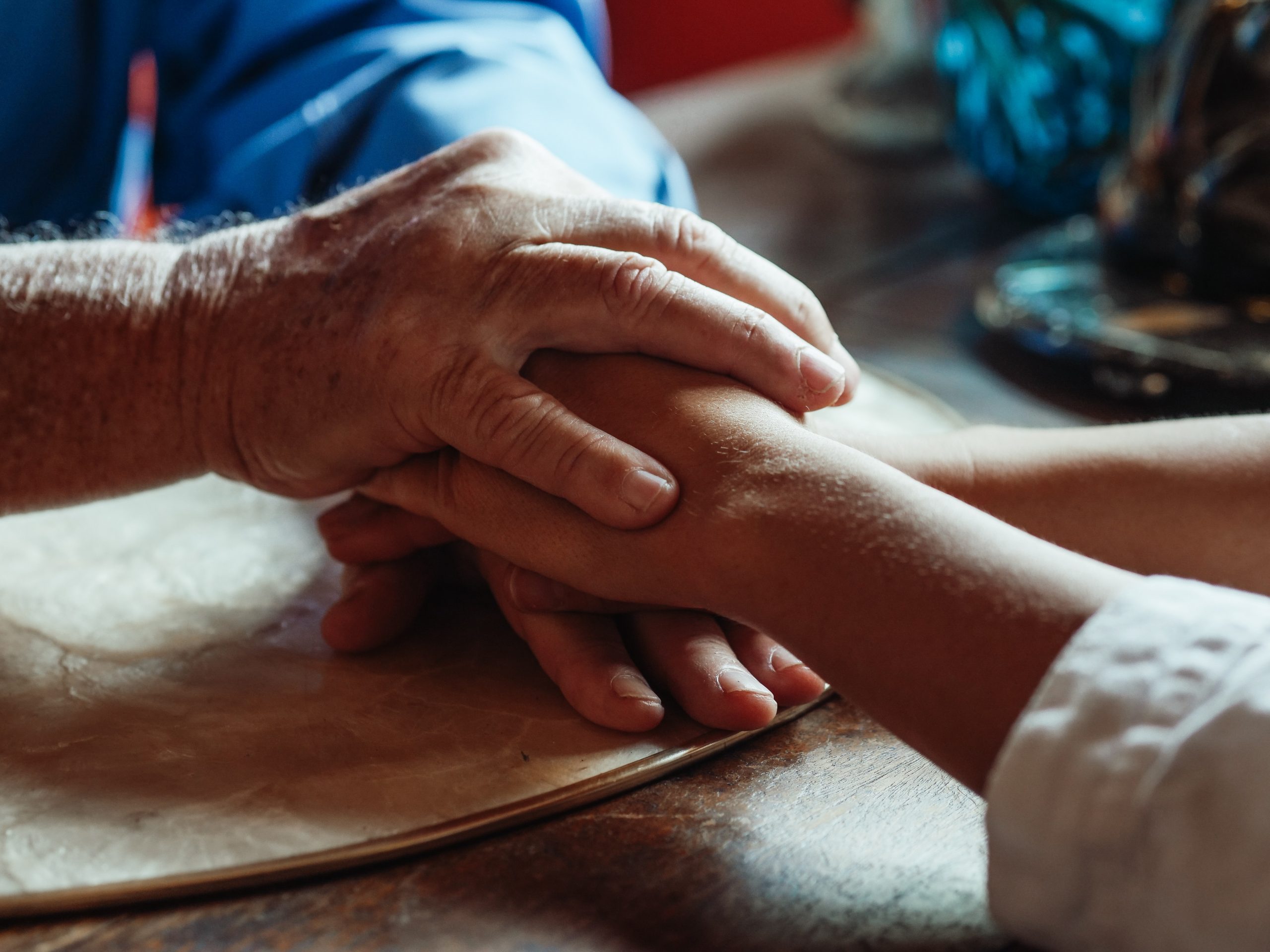 Close up of an elderly man's hands holding a younger woman's hands.